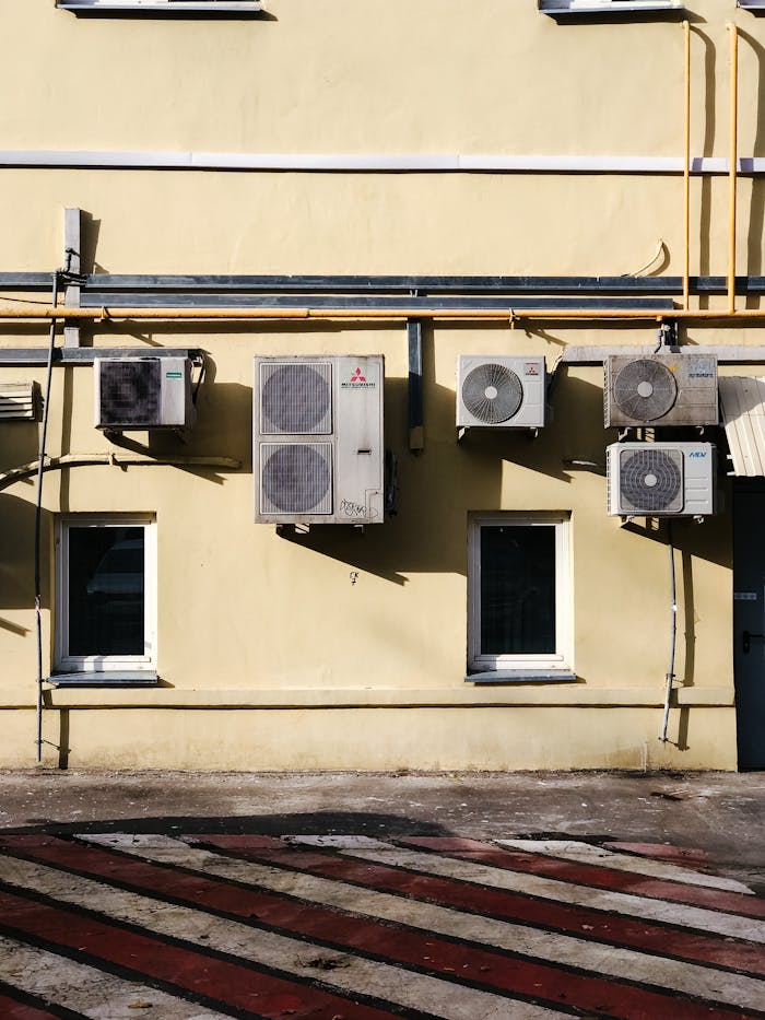 Yellow building facade with multiple air conditioning units mounted on wall.